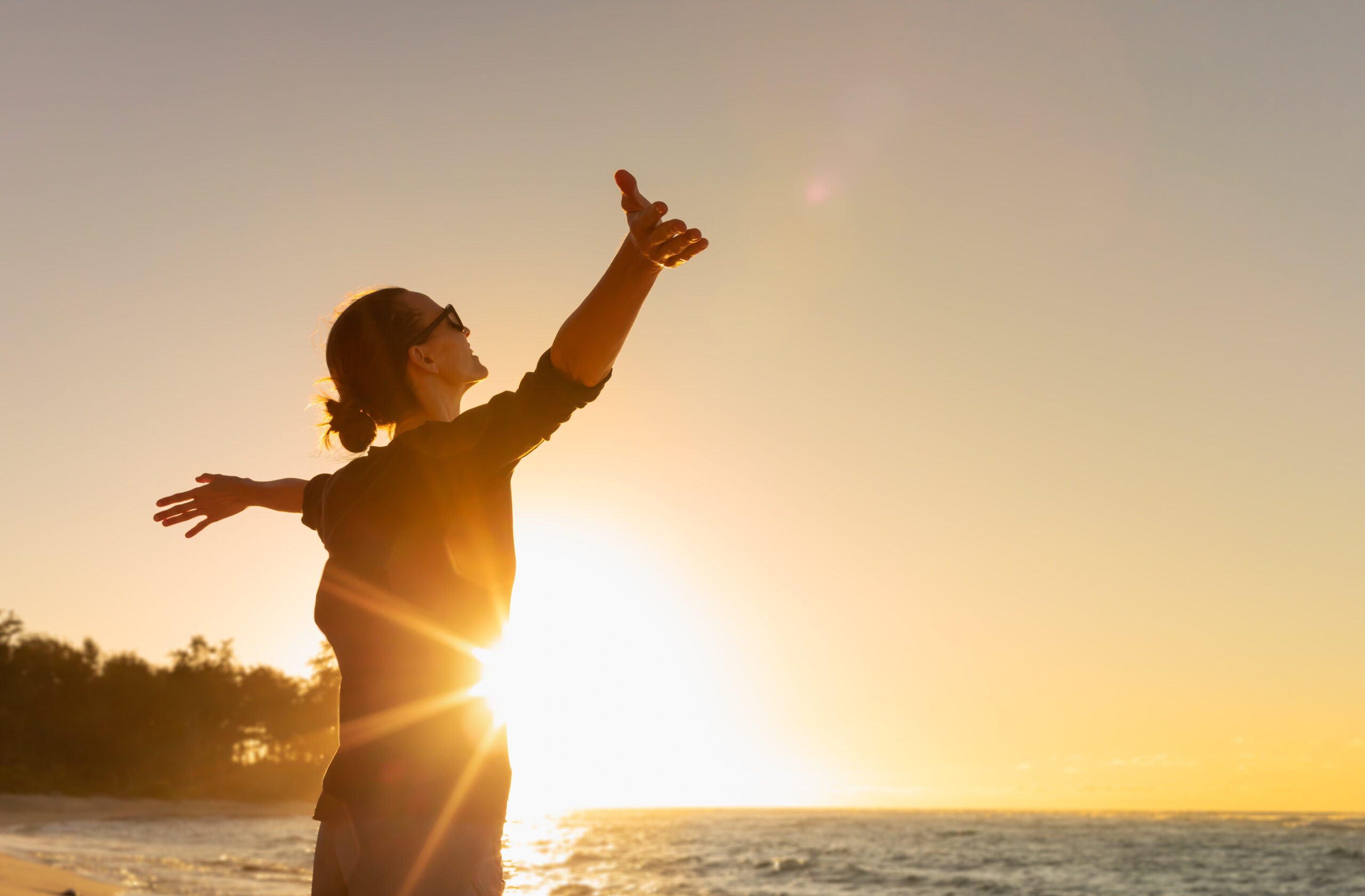 Woman on the beach with her arms outstretched during the sunset.