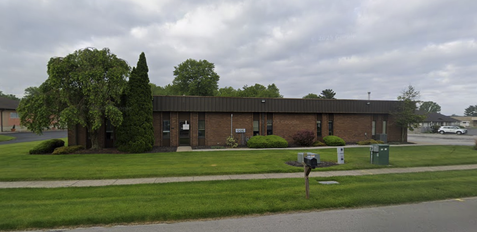 Single-story brick office building with green lawn and trees