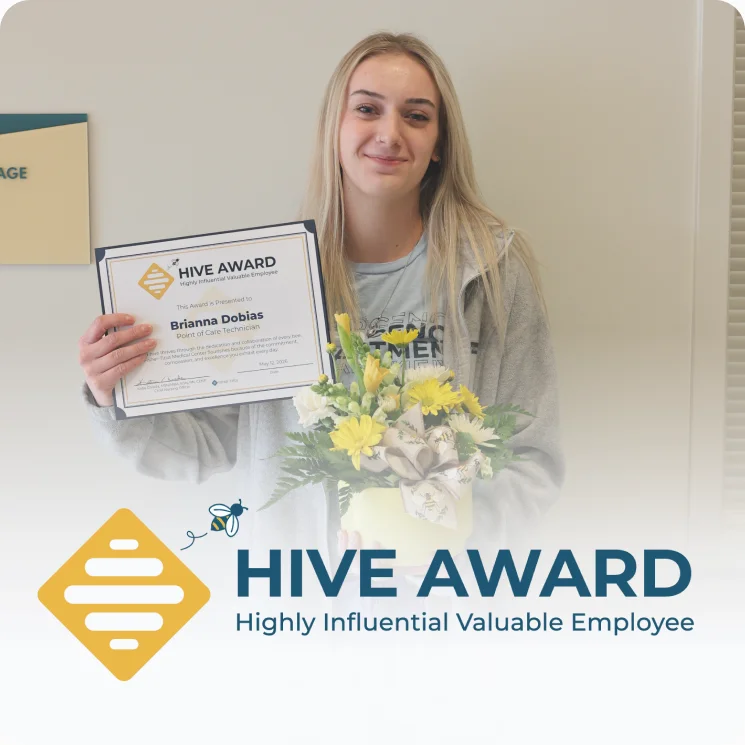A Fisher-Titus employee smiling while holding her HIVE Award certificate and a bouquet of flowers beneath the HIVE Award for Highly Influential Valuable Employee logo